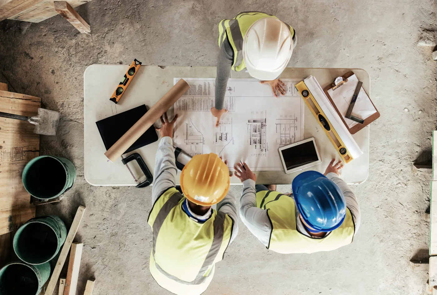 Engineers in hard hats reviewing construction plans, seen from above